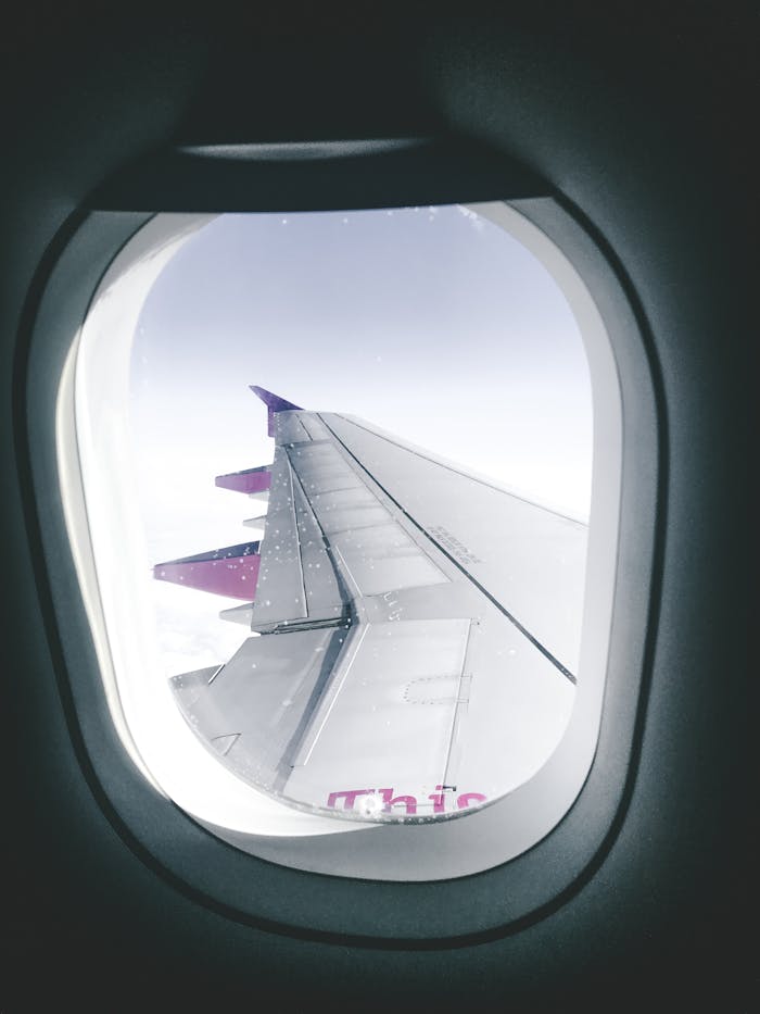 View of an airplane wing through a window, capturing flight over clouds.