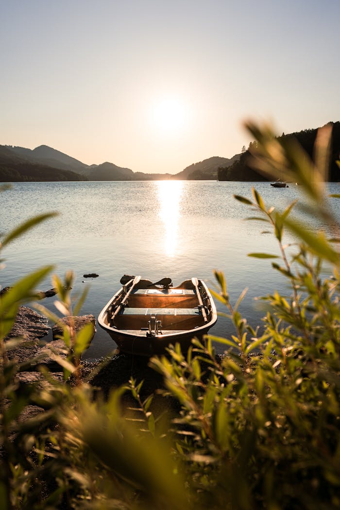 Peaceful sunset at Lake Fuschl in Salzburg with an empty rowboat framed by foliage.