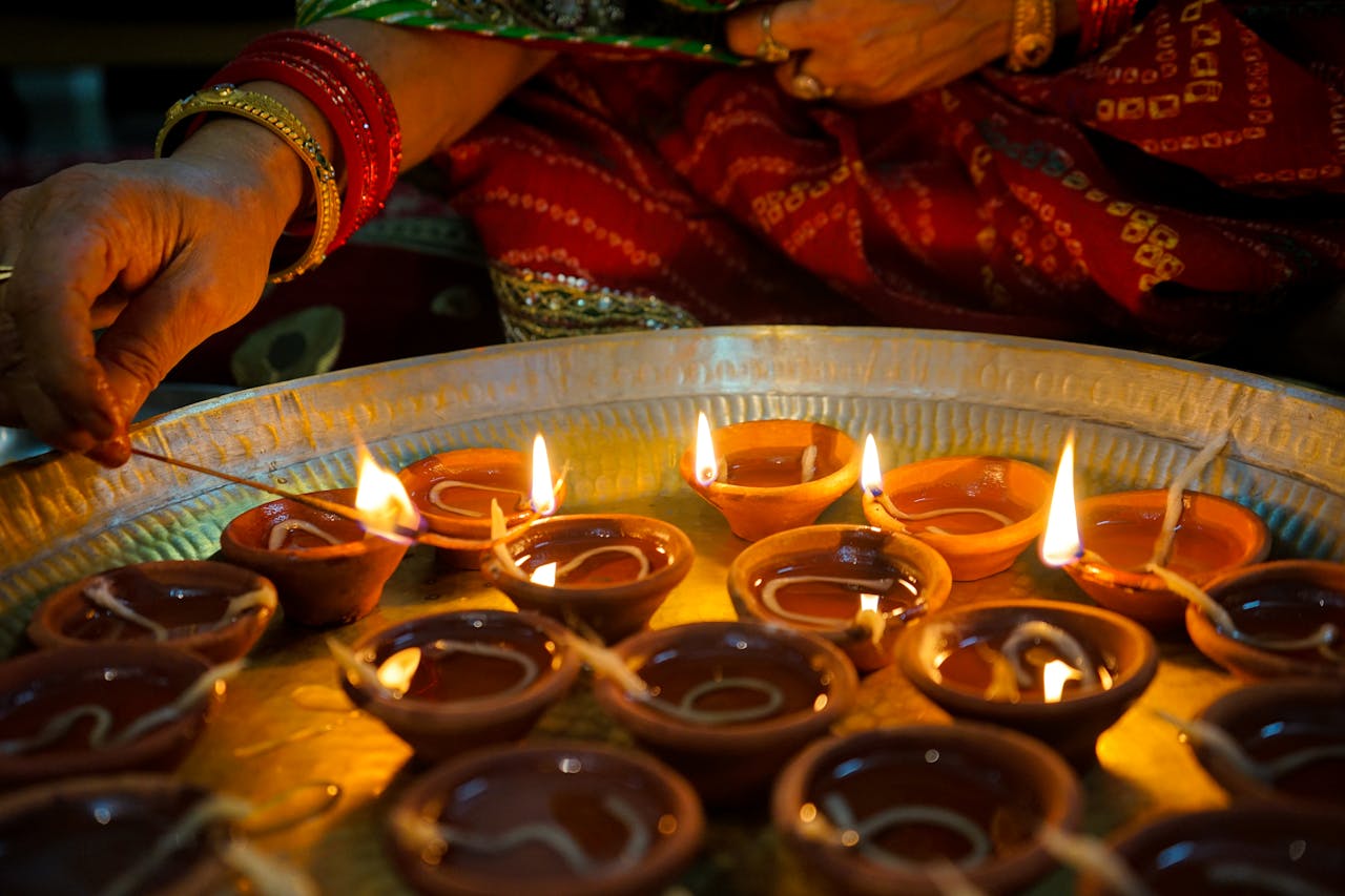 A close-up of hands lighting traditional diya oil lamps during a festive celebration indoors.